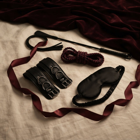 Leren polsboeien, zweepje, zijden touw en blinddoek voor BDSM beginners op crème linnen